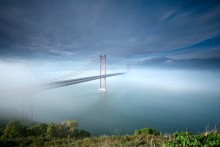 Amo- te , Lisboa! / The 25 de Abril Bridge (Ponte 25 de Abril - "25th of April Bridge"), is a suspension bridge connecting the city of Lisbon, capital of Portugal, to the municipality of Almada on the left (south) bank of the Tejo river. It was inaugurated on August 6, 1966 and a train platform was added in 1999. Because of its similar coloring, it is often compared to the Golden Gate Bridge in San Francisco, USA. In fact, it was built by the same company (American Bridge Company) that constructed the San Francisco-Oakland Bay Bridge and not the Golden Gate, also explaining its similarity in design. With a total length of 2,277 m, it is the 20th largest suspension bridge in the world. The upper platform carries six car lanes, the lower platform two train tracks. Until 1974, the bridge was named Salazar Bridge (Ponte Salazar).