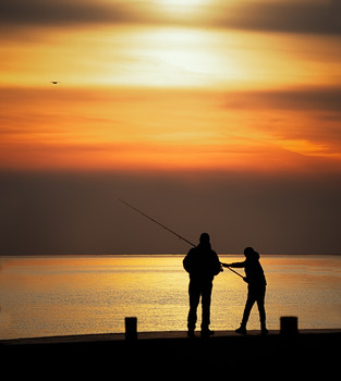  / Father and son fishing off of a pier at sunset.