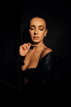 Sensual portrait / A sensual portrait in dark tones of a young girl with dark hair and a pearl necklace, wearing a black leather coat over her bare body and lingerie.