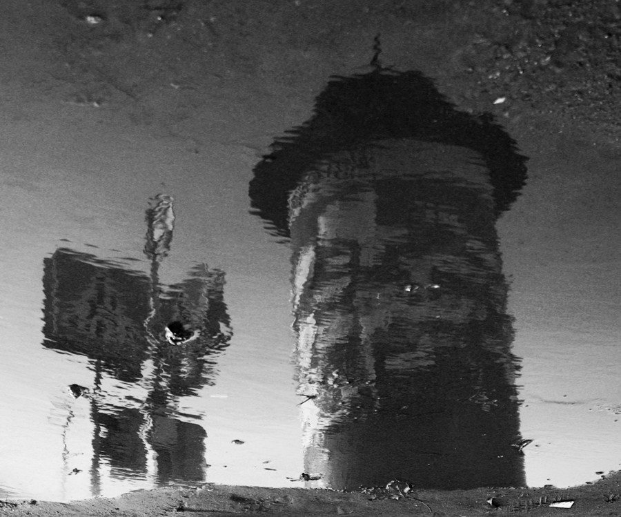 Афишная тумба, световор и дорожный знак, отражающиеся в луже на перекретке в Несвиже